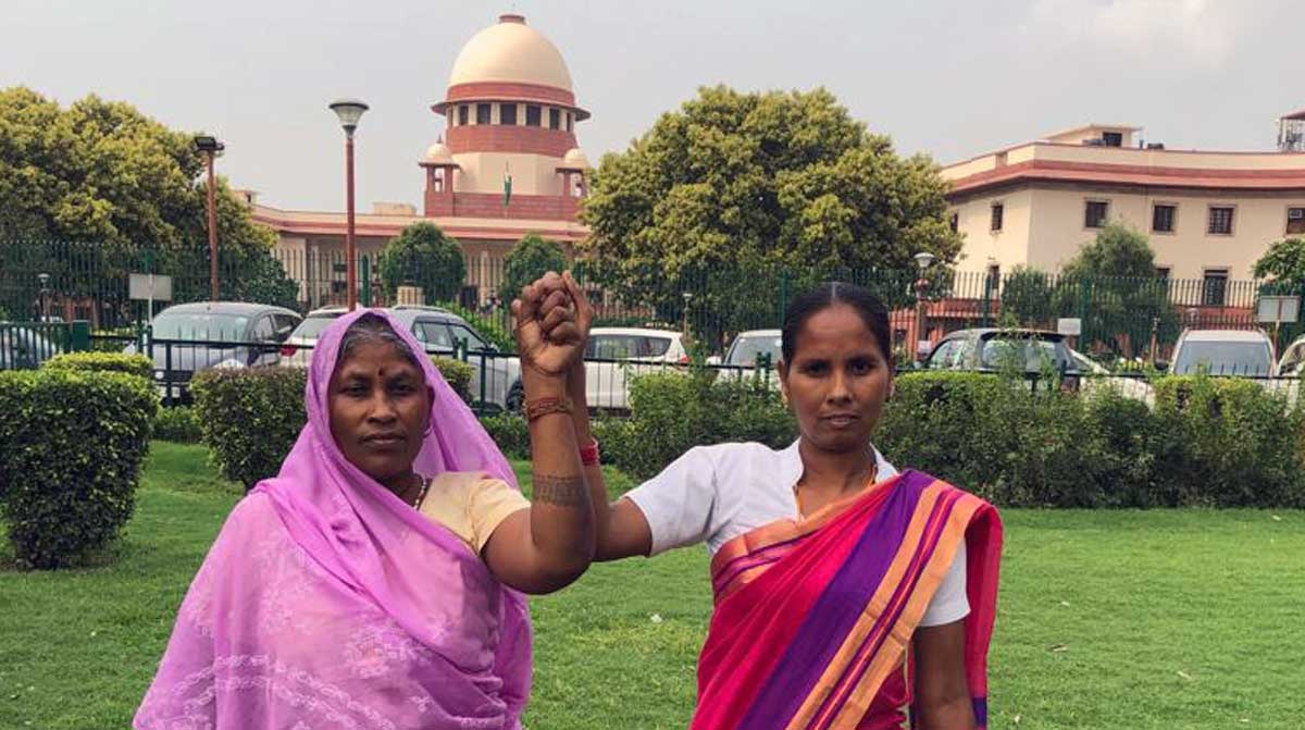 Sokalo Gond of Sonbhadra district and Nivada Rana of Lakhimpur Kheri District stand together outside the Supreme Court of India in Delhi. These two Adivasi women have been an integral part of the legal battle to protect the Forest Rights Act in the Wildlife Trust & Others Vs the Union of India case. Credit: AIUFWP Sokalo Gond of Sonbhadra district and Nivada Rana of Lakhimpur Kheri District stand together outside the Supreme Court of India in Delhi. These two Adivasi women have been an integral part of the legal battle to protect the Forest Rights Act in the Wildlife Trust & Others Vs the Union of India case. Credit: AIUFWP