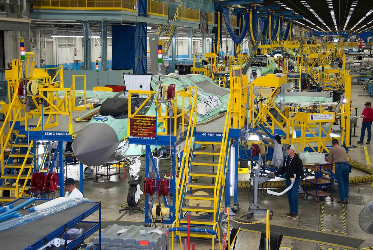 Workers on the production line; fighter plane in background