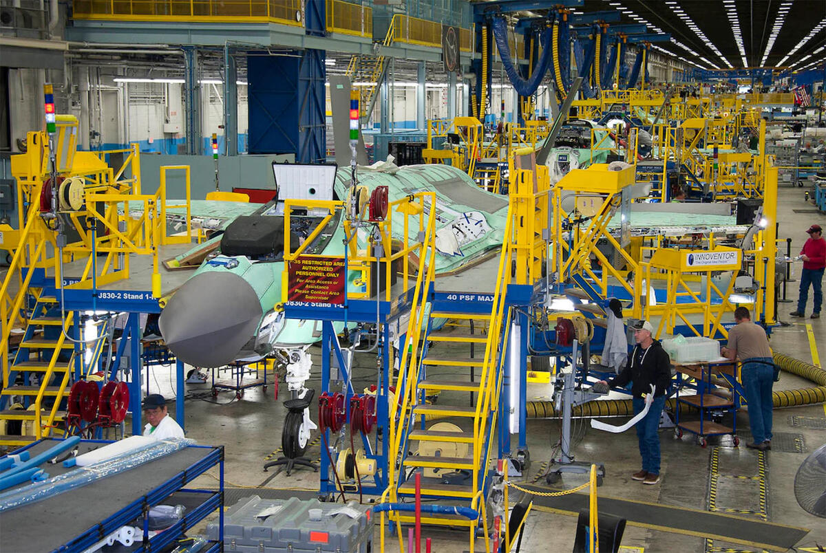 Workers on the production line; fighter plane in background